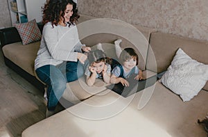 two little girls play on a laptop while lying on the couch mom does her daughter& x27;s hair.