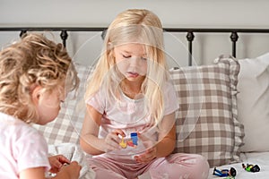 Two little girls playing with toys on the bed in the morning