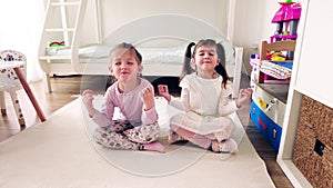 Two little girls practicing yoga. Funny kids doing yoga exercise at home, sitting in a yoga pose
