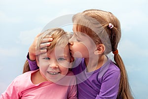 Two little girls, preschoolers, young sisters siblings smliling, laughing. Children kiss on the head concept. Care and love