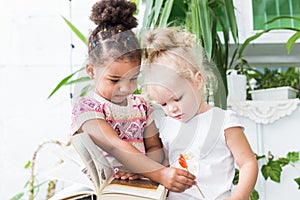 Two little girls read a book on the background of plants in pots