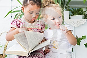 Two little girls read a book on the background of plants in pots
