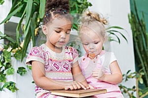 Two little girls read a book on the background of plants in pots