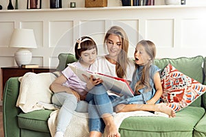 Two little girls are reading a book with their mother