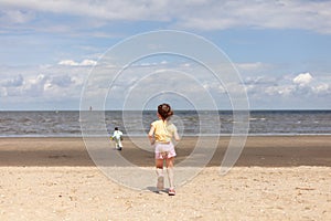 Two little girls run along an empty sandy beach. Cheerful summer vacation during school holidays at sea