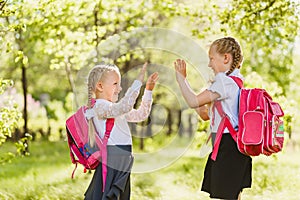 Two little girls schoolgirl with pink backpack and play Patty-cake outdoors