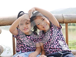 Two little girls, sisters, 2 and 3 years old, smiling and making a heart shape arms together on a bench in the evening sunlight