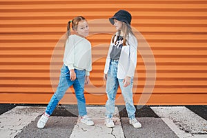 Two little girls sisters dressed kids fashion vogue style clothes posing at camera on the city pedestrian asphalt road near the