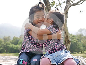 Two little girls, sisters, hugging and kissing on a bench in the evening sunlight - sisters` bond and love