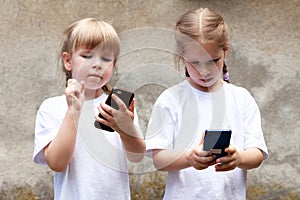 Two little girls, sisters using modern smartphones, young children holding their mobile phones, playing around. New generation