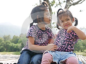 Two little girls, sisters, 3 and 2 years old, kissing on a bamboo bench in the evening sunlight - sisters bond, love, and