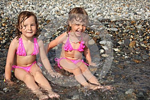 Two little girls sit ashore in water