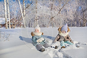 Two little girls sit and play in a snow in a winter