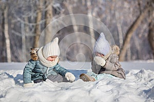 Two little girls sit and play in snowdrift in outdoors