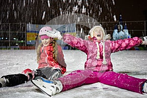 Two little girls sit on skating rink ice in