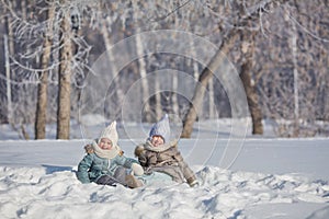 Two little girls sit in snowdrift and fool in winter