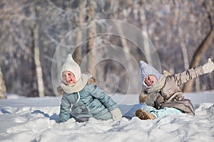 Two little girls sit in snowdrift and make faces in winter