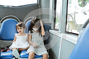 two little girls sitting on a bench playing on the mobile phone on the bus