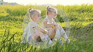 Two little girls sitting on grass talking have fun