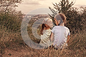 Two little sisters are sitting on a hill above the city