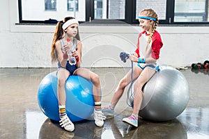 Two little girls in sportswear sitting at fitness studio