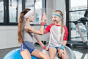 Two little girls in sportswear sitting at fitness studio