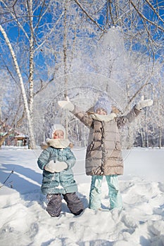 Two little girls stand and throw up a snow in winter
