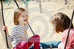 Two little girls are swinging on a swing at the playground