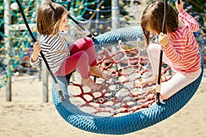 Two little girls are swinging on a swing at the playground