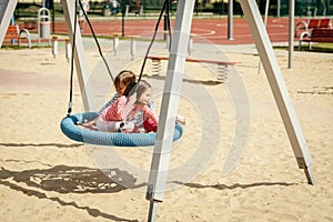 Two little girls are swinging on a swing at the playground