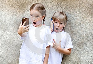 Two little girls with their mobile phones, excited children taking selfies with a smartphone and talking on the phone