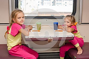 Two little girls on train sitting at the table in the outboard second-class car in the same clothes