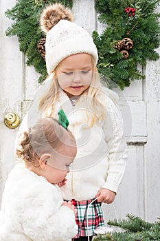 Two little girls in white sweaters standing in front of a rustic white door