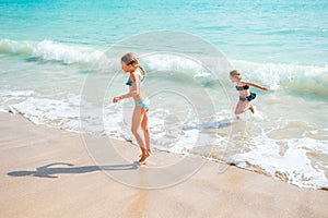 Two little happy girls have a lot of fun at tropical beach playing together at shallow water. Kids splashing.