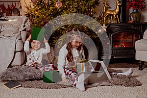 Two little happy girls in pijamas with gift boxes on christmas new year& x27;s eve