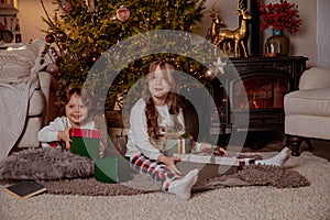 Two little happy girls in pijamas with gift boxes on christmas new year& x27;s eve