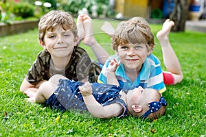Two little happy kid boys with newborn baby girl, cute sister. Siblings on grass in summer or spring in garden. Kids