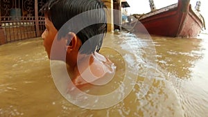 Two little Indian boys bathes in troubled water flooded holy river Ganges Manikarnika Ghat boats on pier Benares