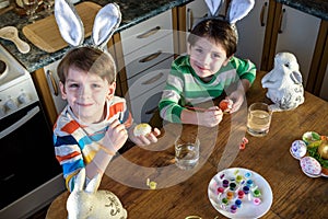 Two little kid boy coloring eggs for Easter holiday in domestic kitchen, indoors. Sibling brothers having fun and celebrating