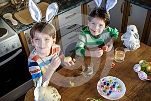 Two little kid boy coloring eggs for Easter holiday in domestic kitchen, indoors. Sibling brothers having fun and celebrating