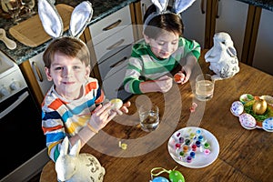 Two little kid boy coloring eggs for Easter holiday in domestic kitchen, indoors. Sibling brothers having fun and celebrating