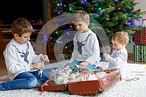 Two little kid boys and adorable baby girl decorating Christmas tree with old vintage toys and balls.