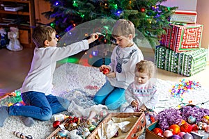 Two little kid boys and adorable baby girl decorating Christmas tree with old vintage toys and balls.