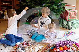 Two little kid boys and adorable baby girl decorating Christmas tree with old vintage toys and balls. Family