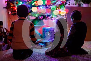 Two little kid boys and adorable toddler girl sitting by Christmas tree with old vintage toys and balls with lots of