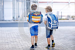 Two little kid boys with backpack or satchel. Schoolkids on the way to school. Healthy adorable children, brothers and