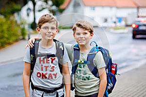 Two little kid boys with backpack or satchel. Schoolkids on the way to school. Healthy adorable children, brothers and