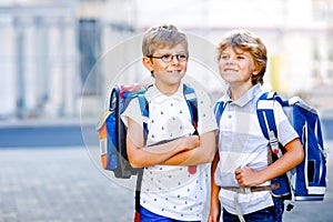 Two little kid boys with backpack or satchel. Schoolkids on the way to school. Healthy adorable children, brothers and