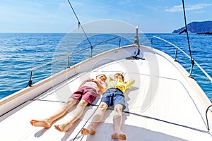 Two little kid boys, best friends enjoying sailing boat trip. Family vacations on ocean or sea on sunny day. Children