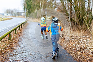 Two little kid boys, best friends riding on scooter in park